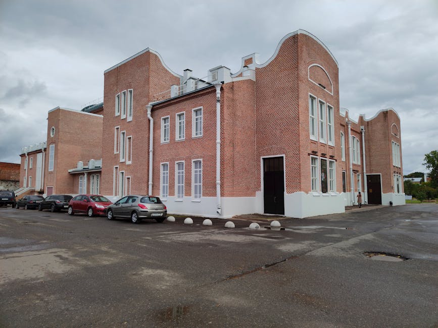 A classic red brick building exterior with cars parked nearby on a cloudy day.