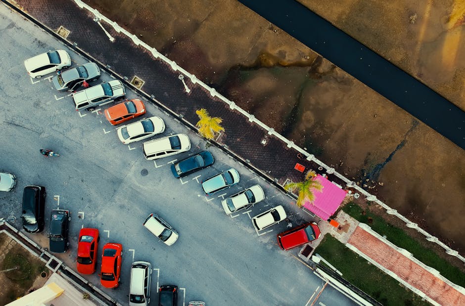 Aerial shot of a parking lot with cars and a pink building, next to a waterway.